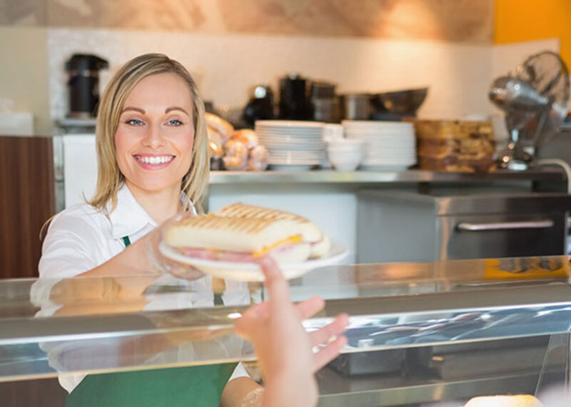 Employee handing customer sandwich in food service operation