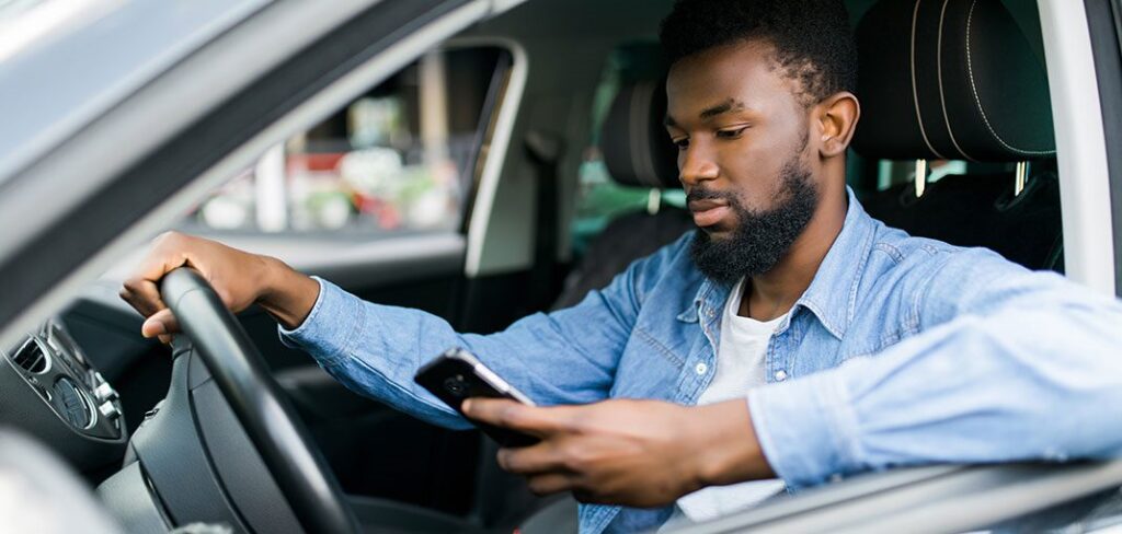 Man in driver's seat of car looking at promotional loyalty app on cell phone.