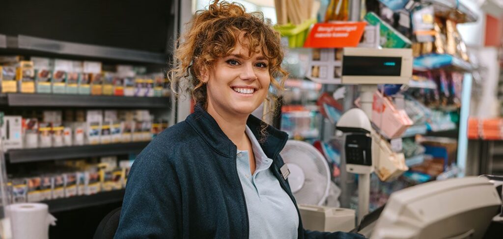 Cashier at convenience retail location checkout smiling and standing in front of POS.