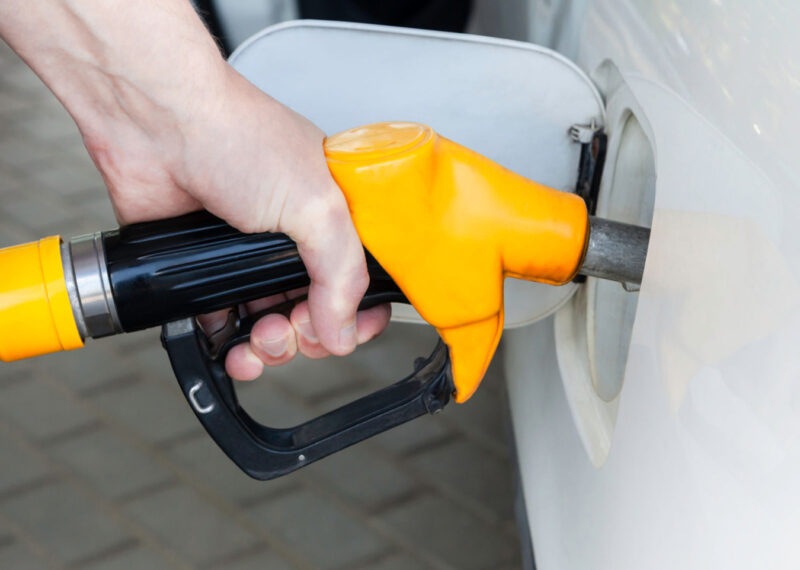 A man pumping fuel with a yellow colored fuel nozzle in a vehicle