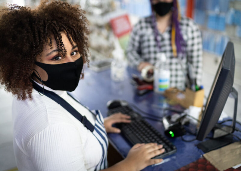Convenience retail industry female cashier wearing a mask using POS to ring up a customer