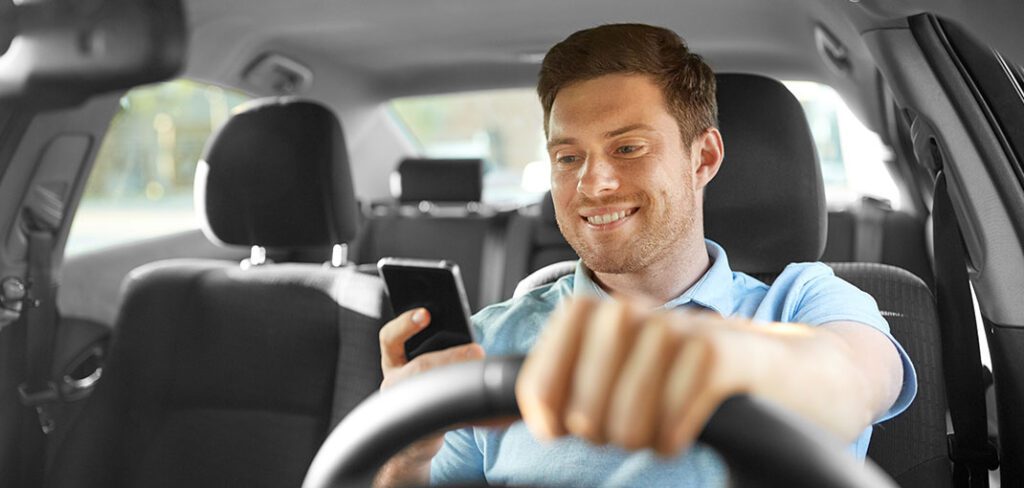 smiling driver driving car and using smartphone