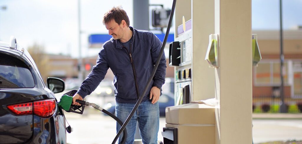 Man standing next to gas pumps at gas station fueling up car.