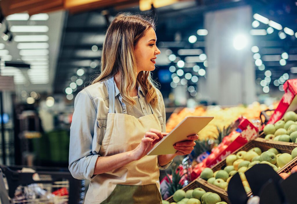 Female grocery store employee using tablet to inventory produce.