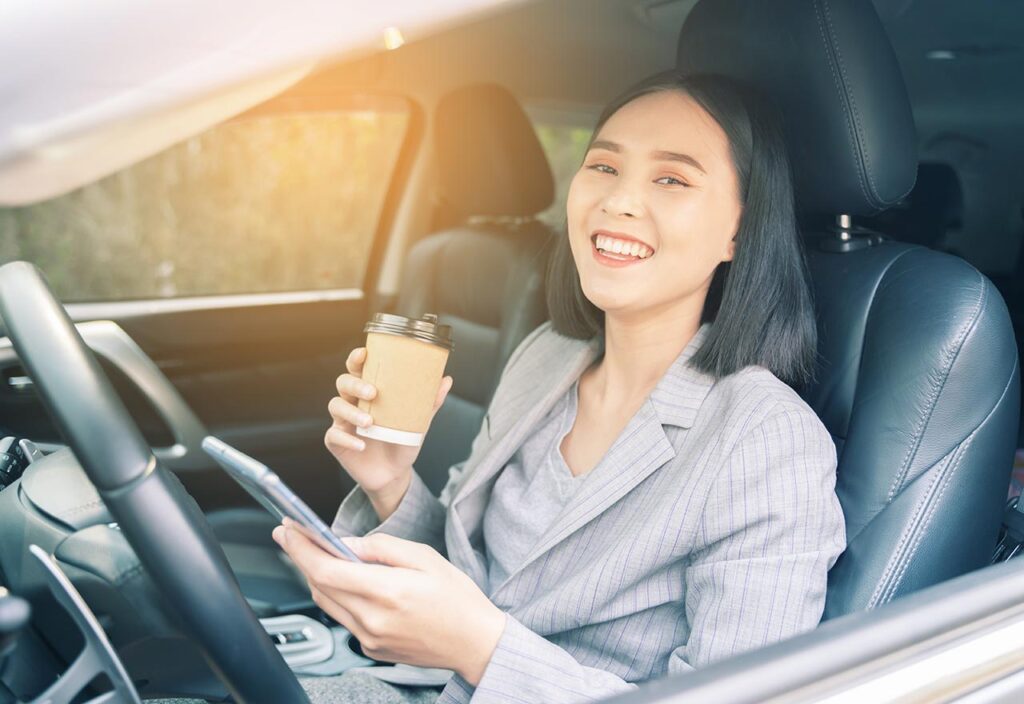 Asian woman sitting in car smiling with phone in her hand