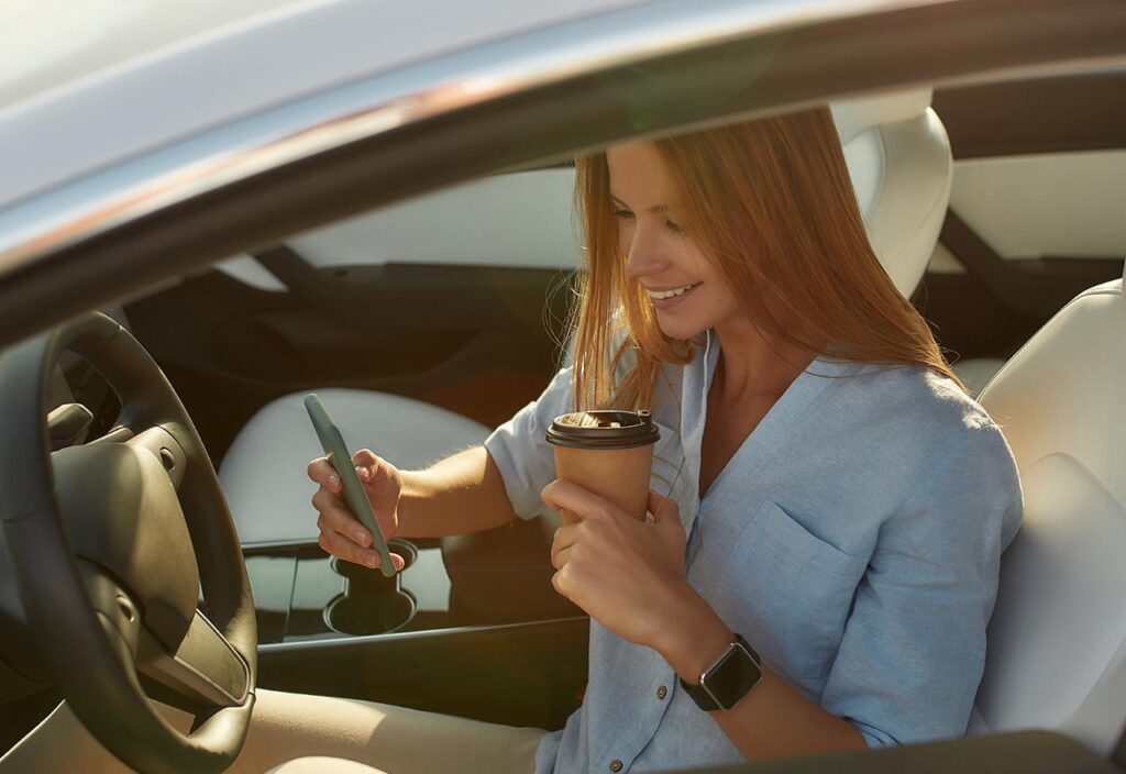 Happy young girl looking into phone sitting in car