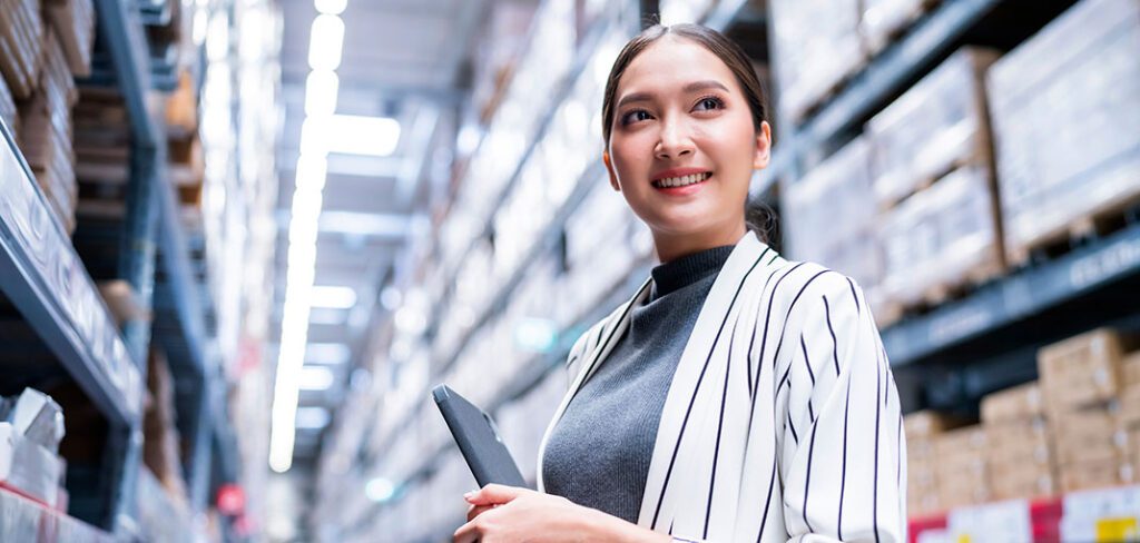 asian woman using digital tablet checking amount of stock product inventory on shelf at distribution warehouse