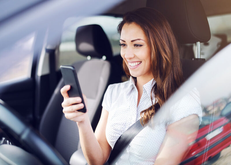 Woman holding cell phone smiling while in drivers seat of car