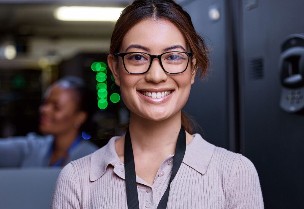 attractive young female programmer working in a server room with her colleague in the background 