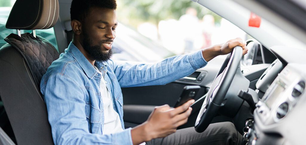 Man parked in car looking at phone using fuel rewards app.