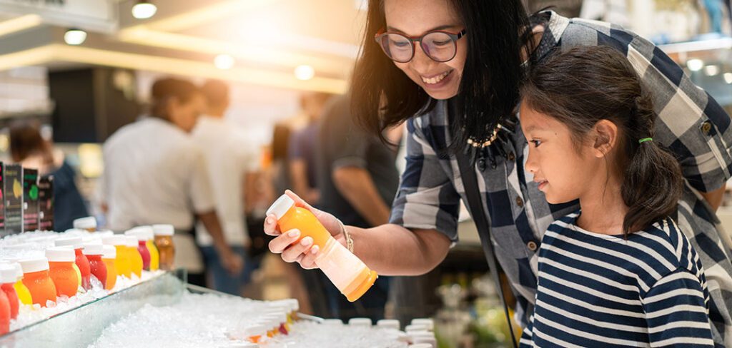 Woman and daughter shopping for orange juice at retail convenience store.