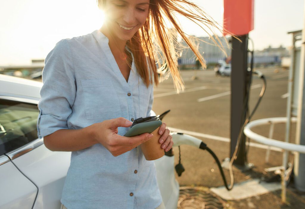 Woman looking into phone while waiting for car charging 