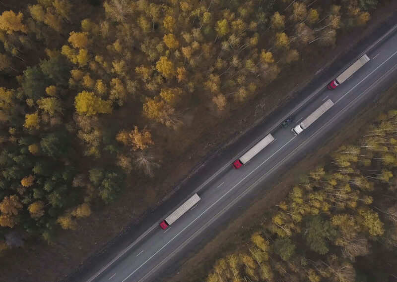 Drone view of sustainable fleet of freight trucks driving on highway through forest