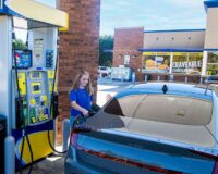 Young woman filling up her car gasoline tank at a convenience store