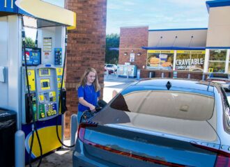 Young woman filling up her car gasoline tank at a convenience store