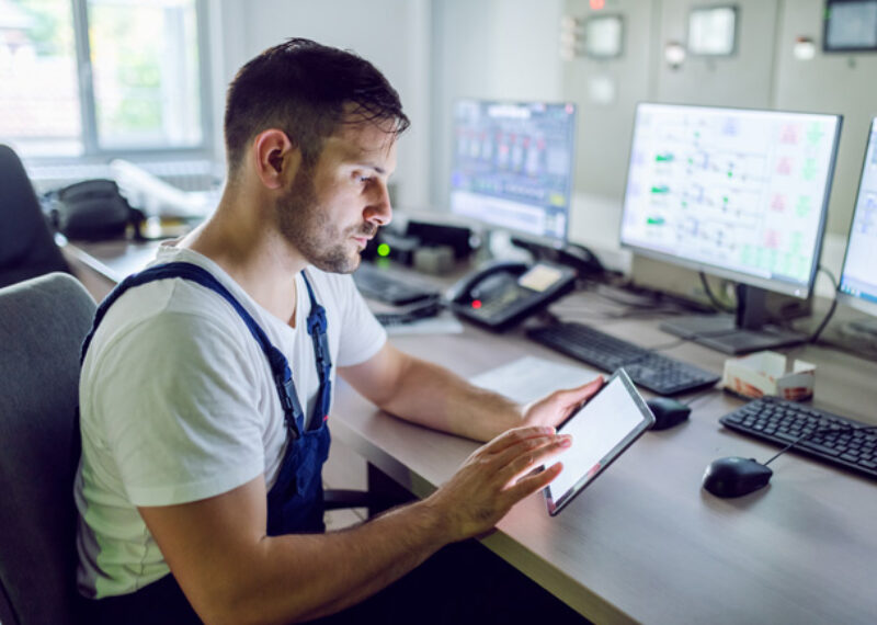 Man looking at fuel logistics schedule on mobile device with several computers in the background