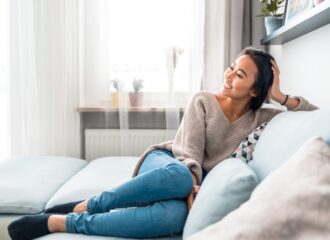 Relaxed smiling Asian woman sitting on sofa warm at home.