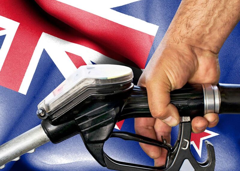 Hand holding gasoline hose against flag of New Zealand