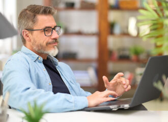 Middle aged man working with laptop at home attending virtual user conference