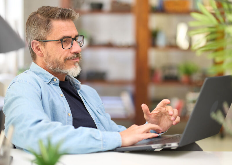 Middle aged man working with laptop at home attending virtual user conference