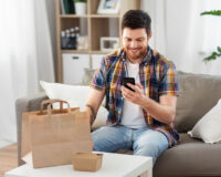 smiling man using smartphone for food delivery at home