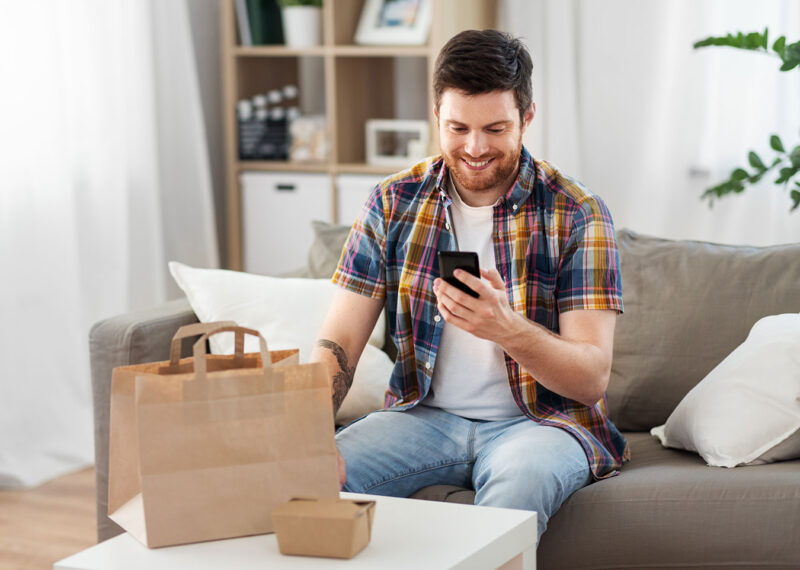 smiling man using smartphone for food delivery at home