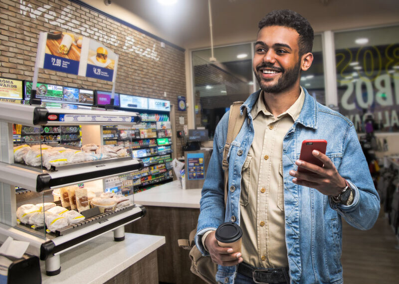 Man holding coffee and his mobile device in a modern convenience store