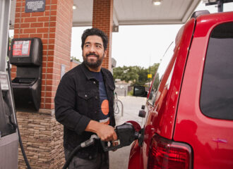 Man standing next to red SUV at convenience store, gas station filling up with fuel