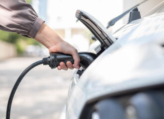 Close up, side view shot, selective focus of a woman's hand grabbing, plugging, holding the EV charger plug handle in front of an electric car. Sustainable energy