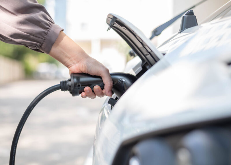 Close up, side view shot, selective focus of a woman's hand grabbing, plugging, holding the EV charger plug handle in front of an electric car. Sustainable energy