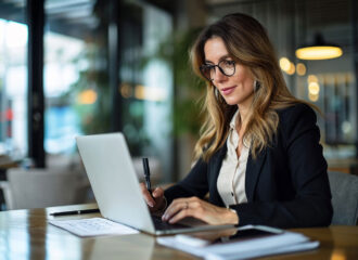 Busy mature mid aged business woman professional in her 40s writing notes finance report overview, lawyer checking document, working on laptop computer device sitting at desk in office