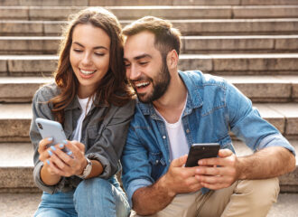 Two individuals sitting on outdoor steps, both engaged with their smartphones.