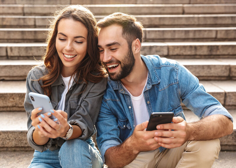 Two individuals sitting on outdoor steps, both engaged with their smartphones.