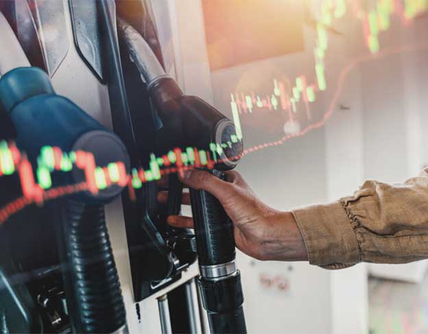 Person selecting a fuel pump nozzle at a gas station with a digital stock market chart overlay representing fuel pricing trends.