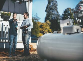 Two men discussing propane delivery operations beside a propane tank and fuel truck, reviewing plans to modernize commercial fuel services.