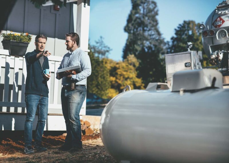 Two men discussing propane delivery operations beside a propane tank and fuel truck, reviewing plans to modernize commercial fuel services.
