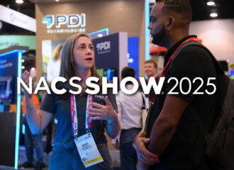 PDI Technologies employee speaking with an attendee at the NACS Show booth, with PDI branding and displays visible in the background.