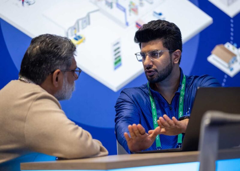 Two professionals in discussion at the PDI Technologies booth during NACS Show 2025 in Chicago.