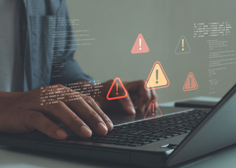 Cybersecurity threat alerts appearing on a laptop screen as a user types, representing malware detection and cyber risk monitoring.