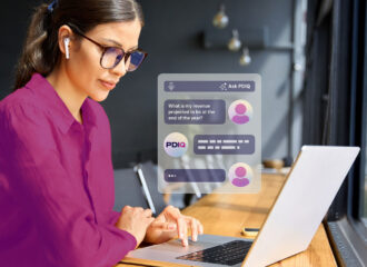 Woman in a magenta blouse works on a laptop while an Ask PDIQ chat interface overlays the scene, showing a user asking 'What is my revenue projected to be at the end of the year?' with PDIQ responding with data insights.