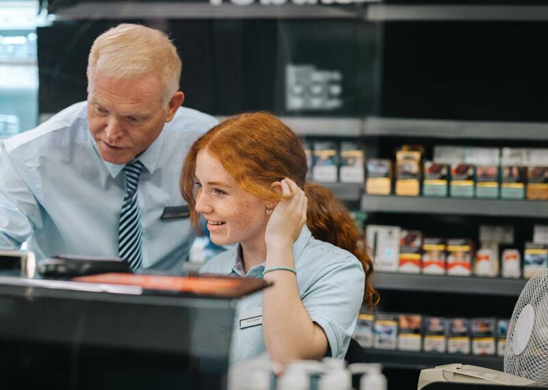 Convenience store manager helping a new employee at the checkout counter