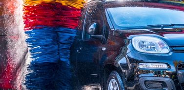 Car passing through a car wash with colorful brushes, illustrating a car wash subscription