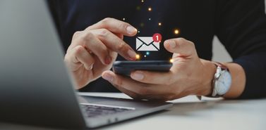 Hand holding a smartphone with email and messaging icons, representing multichannel customer outreach