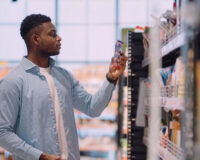Shopper looking at a packaged product on a convenience store shelf, where electronic shelf labels keep pricing accurate