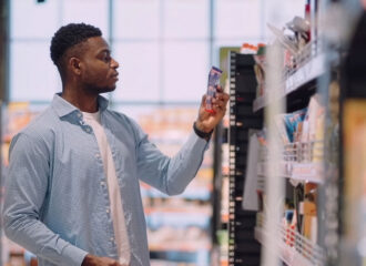 Shopper looking at a packaged product on a convenience store shelf, where electronic shelf labels keep pricing accurate