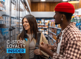 Two shoppers chat in front of a convenience store cooler aisle, with a 